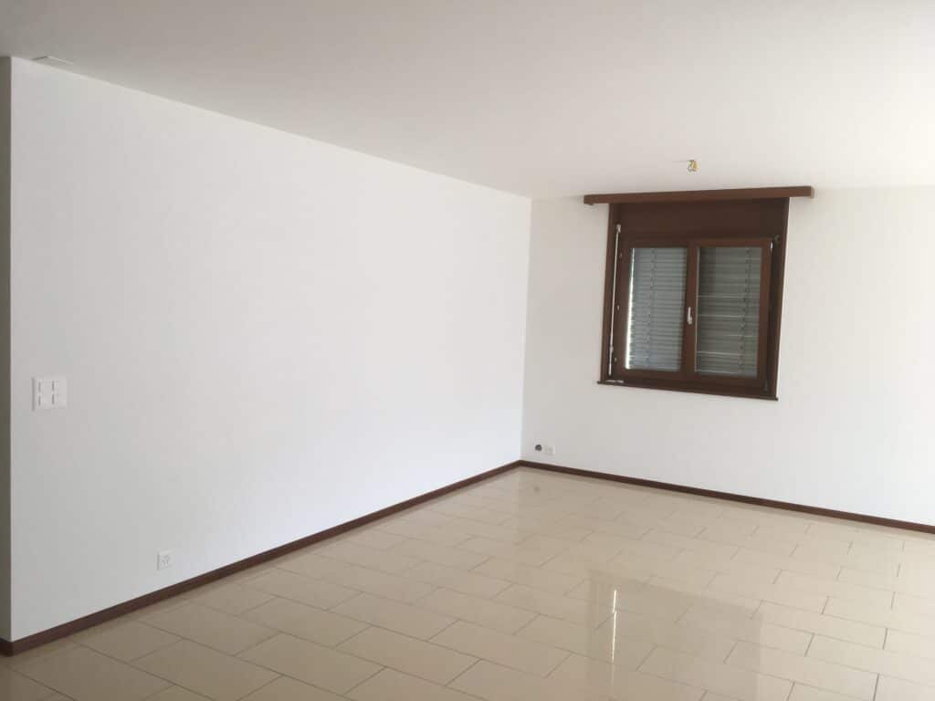 Salle lumineuse avec mur blanc et fenêtre.