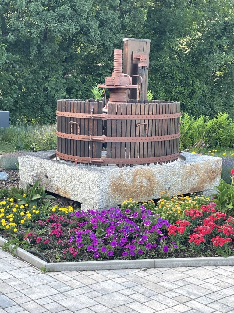 Ancien pressoir en bois entouré de fleurs colorées.