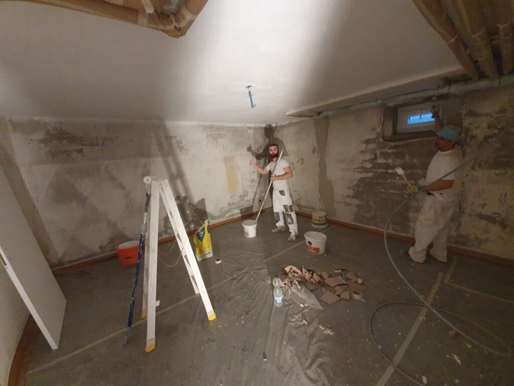 Deux ouvriers peignent le plafond d'une pièce.
