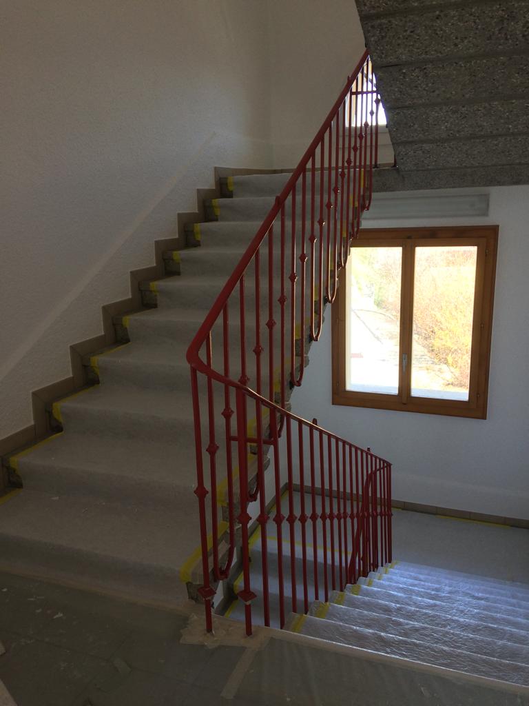 Escalier avec rampe rouge et fenêtre en arrière-plan.