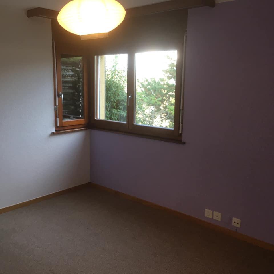 Chambre vide avec mur violet et fenêtre.