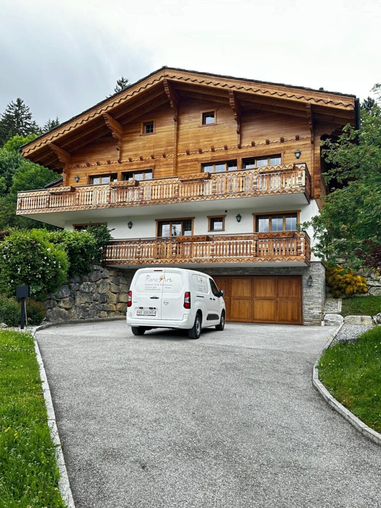 Chalet en bois avec véhicule devant, paysage verdoyant.